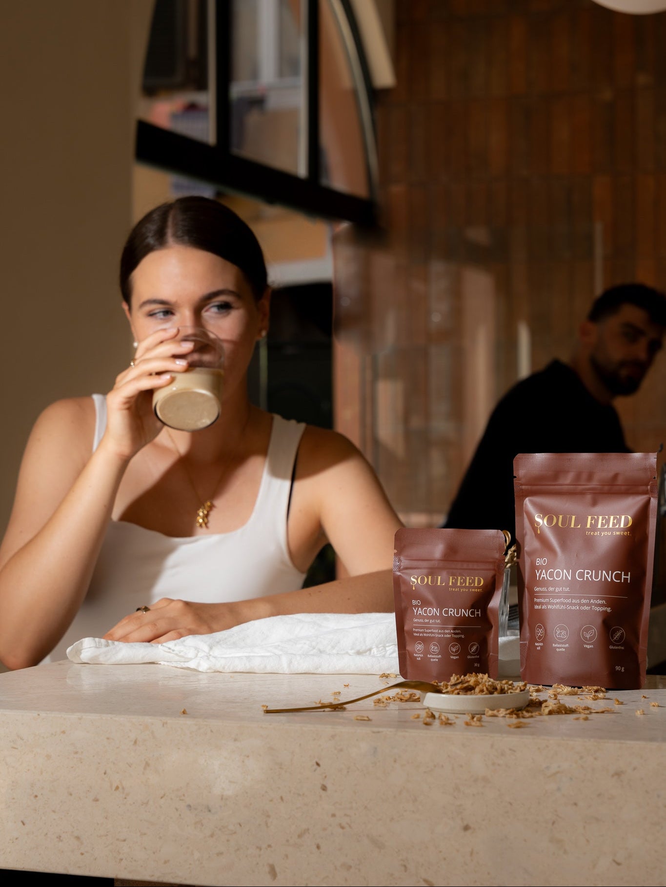 Soul Feed Yacon Crunch an der Theke. Eine Frau und ein Mann schauen auf die 30g und 90g Packung.