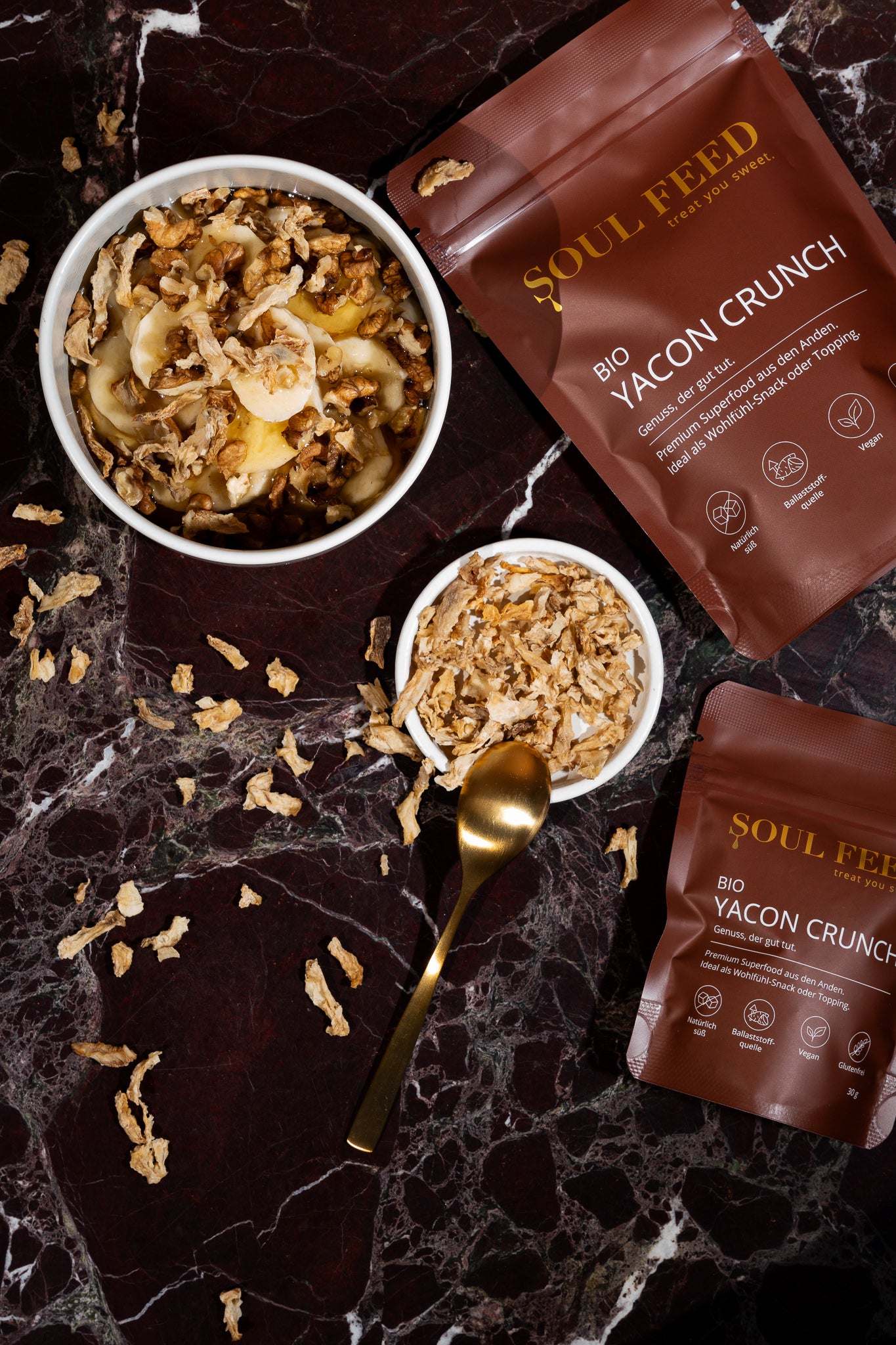 Packung Soul Feed Bio Yacon Crunch neben einer Schale mit Yacon Crunch auf einem Marmortisch.