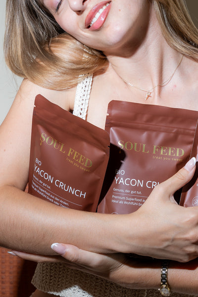 Bio Yacon Crunch Verpackungen mit strahlender Frau im Hintergrund.